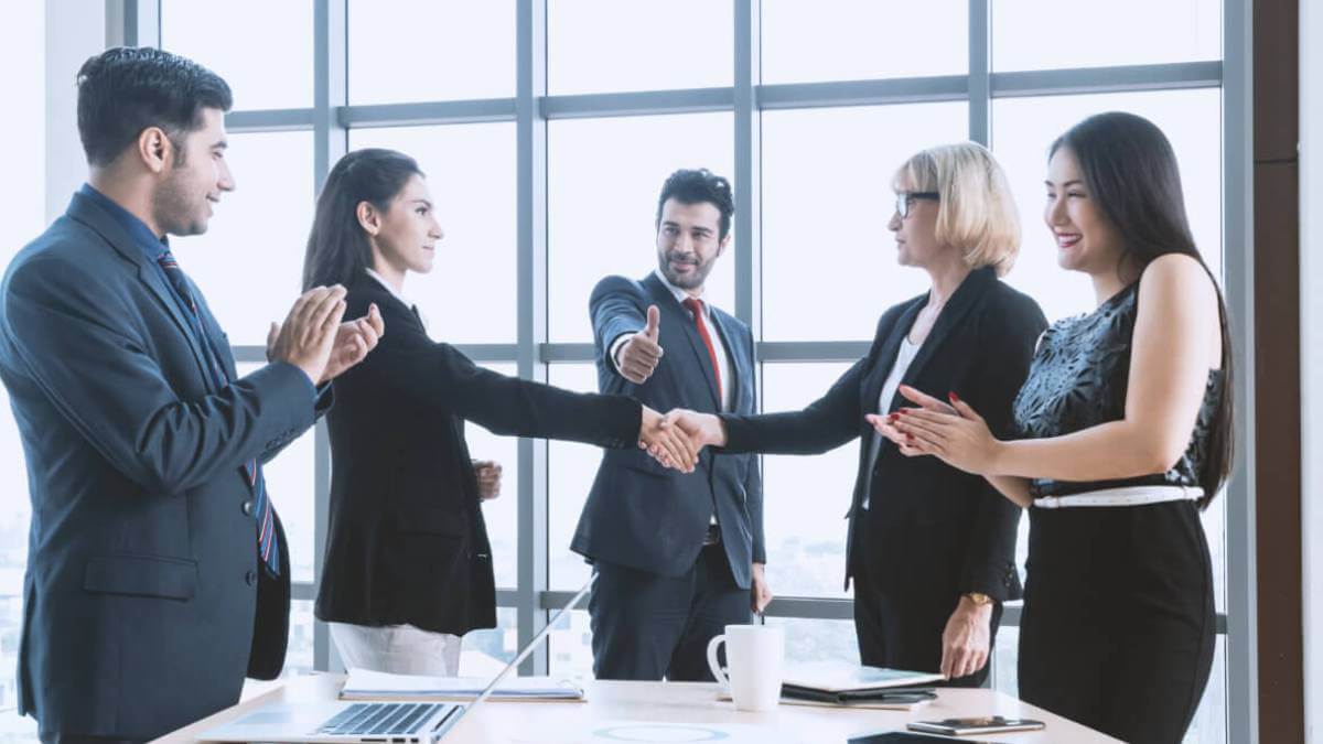 offshoring vs. nearshoring Five business executives are inside a meeting room, discussing offshoring vs. nearshoring.