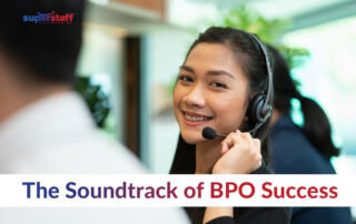 A friendly female call center agent with long dark hair and braces, wearing a headset and smiling while assisting a customer. She is seated in a modern, well-lit call center environment with other agents working in the background. The SuperStaff Outsourcing logo is in the upper left corner. The text overlay reads, 'The Soundtrack of BPO Success,' with 'Soundtrack' in bold blue and 'BPO Success' in bold red, emphasizing the role of call center professionals in delivering excellent customer service.
